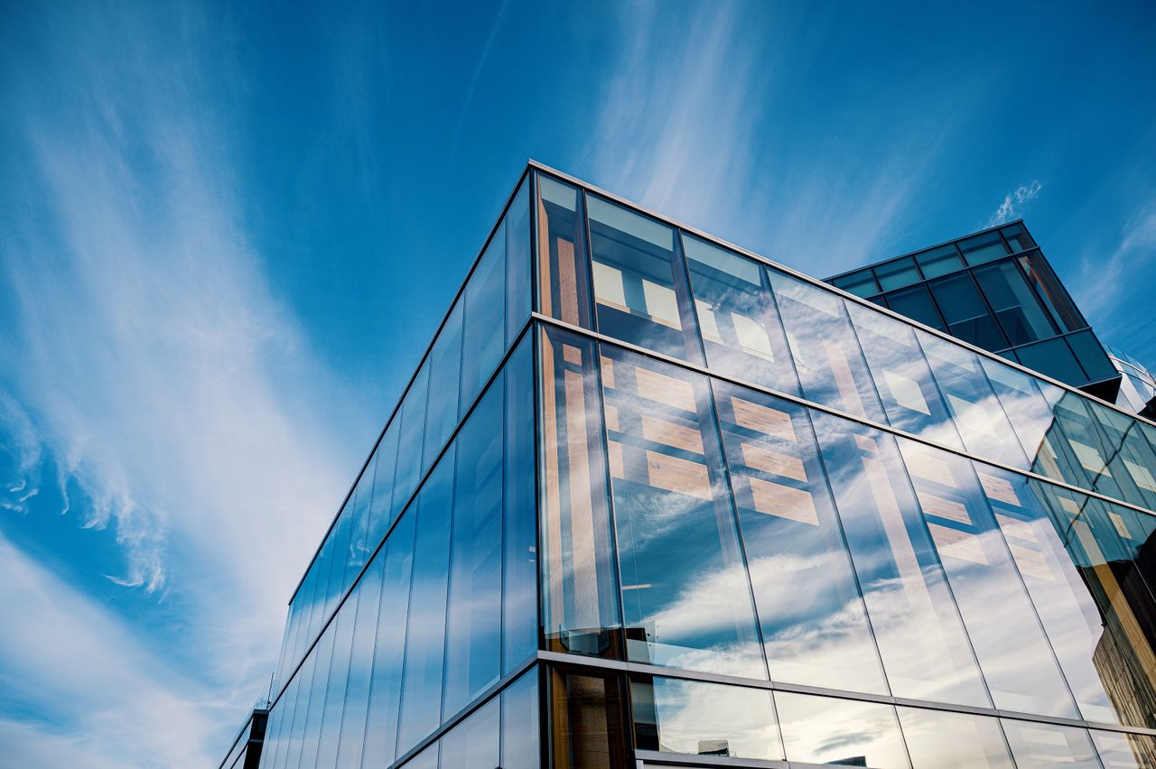 The Art of Drawing Readers In: Your attractive post title goes here Sleek glass facade reflecting clouds in a modern architectural design under a bright blue sky.